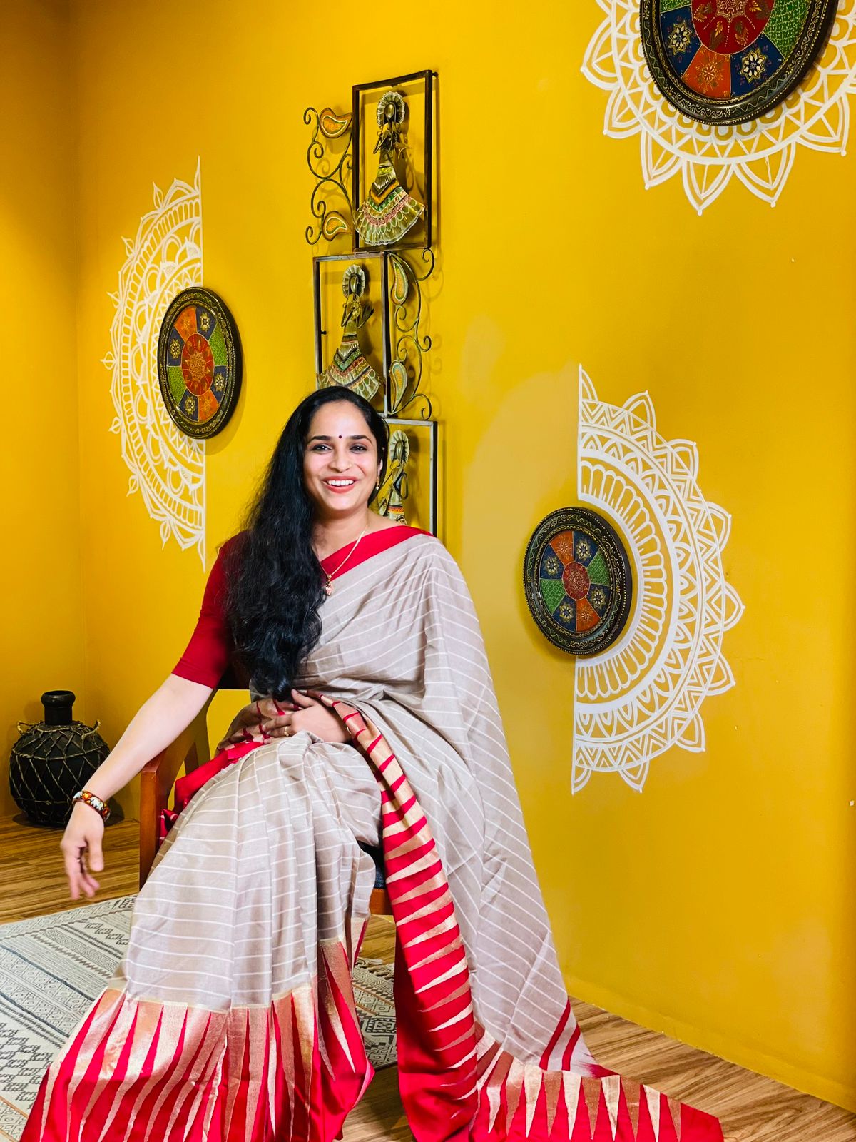 Akhila seated in a red and cream sari in a warm yellow room